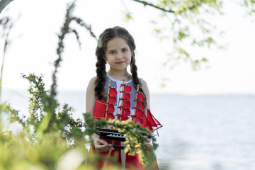 Portrait of a happy little girl by the lake. In her hands she holds a toy sailboat with scarlet sails.