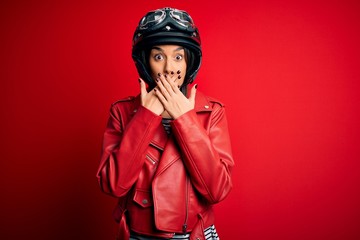 Young beautiful brunette motorcyclist woman wearing motorcycle helmet and red jacket shocked...