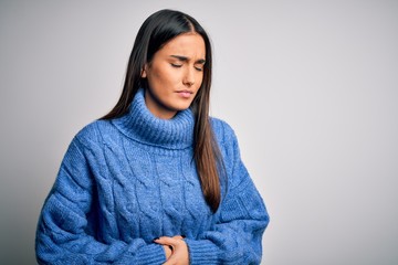 Young beautiful brunette woman wearing casual turtleneck sweater over white background with hand on stomach because indigestion, painful illness feeling unwell. Ache concept.