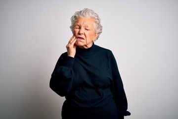 Senior beautiful woman wearing casual black sweater standing over isolated white background touching mouth with hand with painful expression because of toothache or dental illness on teeth. Dentist