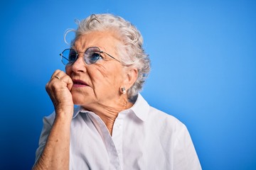 Senior beautiful woman wearing elegant shirt and glasses over isolated blue background looking stressed and nervous with hands on mouth biting nails. Anxiety problem.