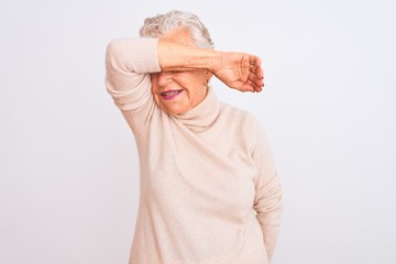 Senior grey-haired woman wearing turtleneck sweater standing over isolated white background covering eyes with arm smiling cheerful and funny. Blind concept.