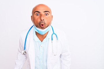 Middle age doctor man wearing stethoscope and mask over isolated white background afraid and shocked with surprise expression, fear and excited face.