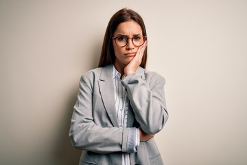 Young beautiful brunette businesswoman wearing jacket and glasses over white background thinking looking tired and bored with depression problems with crossed arms.