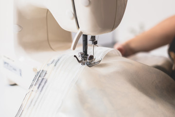 Process of sewing the curtains at home, close up of curtain tape on the sewing machine, hemming, tailoring, repairing and stitching cloth and dress, with the hand of female dressmaker in background