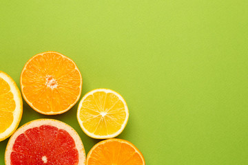 Citruses fruits on green background with copyspace, fruit flatlay, summer minimal compositon with grapefruit, lemon, mandarin and orange