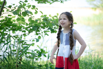 Portrait of a beautiful little girl with long hair on a background of nature on a sunny day.