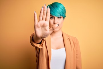 Young beautiful woman with blue fashion hair wearing casual jacket over yellow background doing...