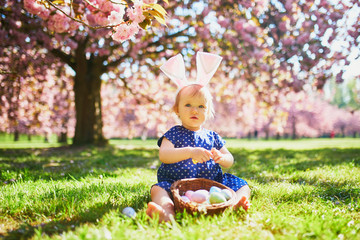 Cute one year old girl sitting on the grass and eating strawberries