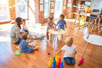 Beautiful teacher and group of toddlers playing around lots of toys at kindergarten