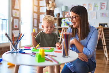 Young caucasian child playing at playschool with teacher. Mother and son at playroom drawing a draw with color pencils