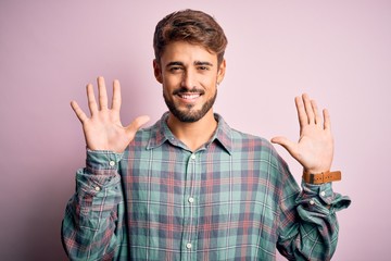 Fototapeta premium Young handsome man with beard wearing casual shirt standing over pink background showing and pointing up with fingers number ten while smiling confident and happy.
