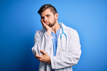 Young blond doctor man with beard and blue eyes wearing white coat and stethoscope thinking looking tired and bored with depression problems with crossed arms.