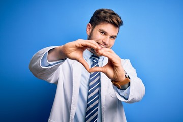 Young blond therapist man with beard and blue eyes wearing coat and tie over background smiling in love doing heart symbol shape with hands. Romantic concept.