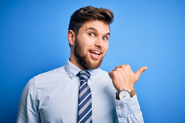 Young blond businessman with beard and blue eyes wearing elegant shirt and tie standing smiling with happy face looking and pointing to the side with thumb up.