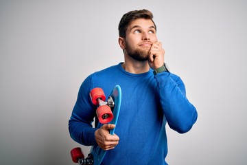 Young blond skeater man with beard and blue eyes holding skate over white background serious face...