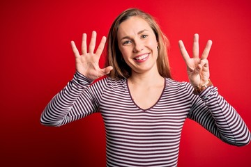 Young beautiful blonde woman wearing casual striped t-shirt over isolated red background showing and pointing up with fingers number eight while smiling confident and happy.