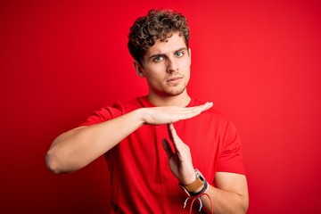Young blond handsome man with curly hair wearing casual t-shirt over red background Doing time out...