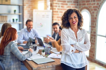 Group of business workers working together. Middle age beautiful businesswoman standing smiling happy looking at the camera at the office