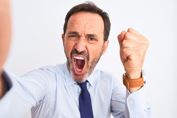 Middle age businessman wearing tie make selfie standing over isolated white background annoyed and frustrated shouting with anger, crazy and yelling with raised hand, anger concept