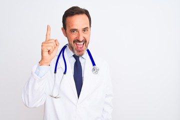 Fototapeta premium Middle age doctor man wearing coat and stethoscope standing over isolated white background pointing finger up with successful idea. Exited and happy. Number one.
