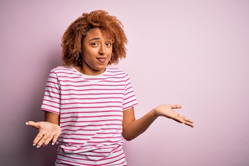 Young beautiful African American afro woman with curly hair wearing casual striped t-shirt clueless...
