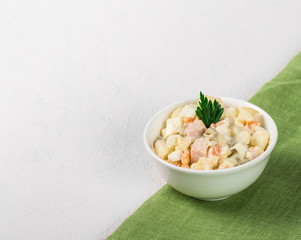 Traditional Russian Olivier Salad with chicken, eggs, potatoes, pickles, green peas, carrots and parsley in a Cup on a light background