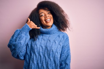 Young beautiful african american woman with afro hair wearing winter sweater over pink background smiling doing phone gesture with hand and fingers like talking on the telephone. Communicating