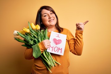 Young beautiful plus size woman celebrating mothers day holding love mom message very happy pointing with hand and finger to the side