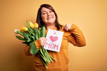 Young beautiful plus size woman celebrating mothers day holding love mom message with surprise face pointing finger to himself