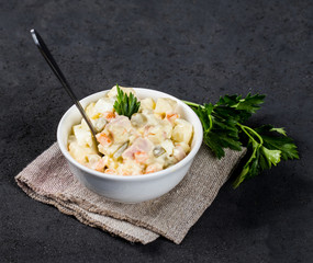 Traditional Russian Olivier Salad with chicken, eggs, potatoes, pickles, green peas, carrots and parsley in a Cup on a light background