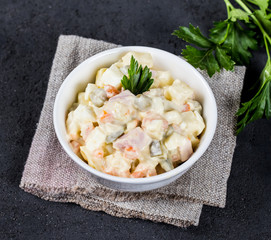 Traditional Russian salad olivier with chicken, eggs, potatoes, pickles, green peas, carrots and parsley in a Cup on a dark background