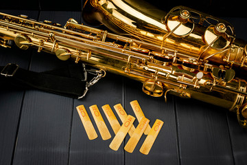 Reeds of mouth piece of a saxophone with a tenor saxophone on gray wooden background