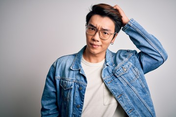Young handsome chinese man wearing denim jacket and glasses over white background confuse and...