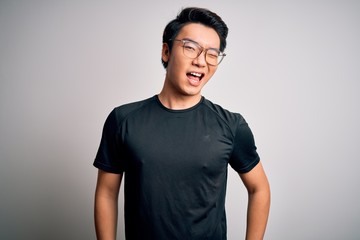 Young handsome chinese man wearing black t-shirt and glasses over white background winking looking at the camera with sexy expression, cheerful and happy face.
