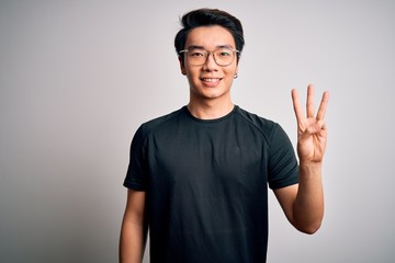 Young handsome chinese man wearing black t-shirt and glasses over white background showing and pointing up with fingers number three while smiling confident and happy.