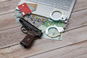 Handcuffs, US dollars and Euro banknotes, credit cards, Makarov 9 mm gun and laptop on wooden table. Piracy, internet hacking and punishment for cybercrime concept.