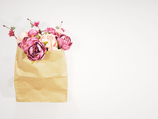 Paper shopping bag with flower in it presented on white background. Ecology concept. Peonies in a brown kraft bag. Spring sale, shop, greeting card. Copy space. Floral gift idea. Springtime holiday.
