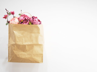 Paper shopping bag with flower in it presented on white background. Ecology concept. Peonies in a...