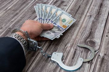 A man's hand in handcuffs and US dollars banknotes on wooden table. Corruption or economic crime...