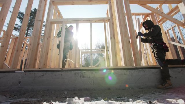 Sliding view from below of framers working at frame residential house building. Sunny day