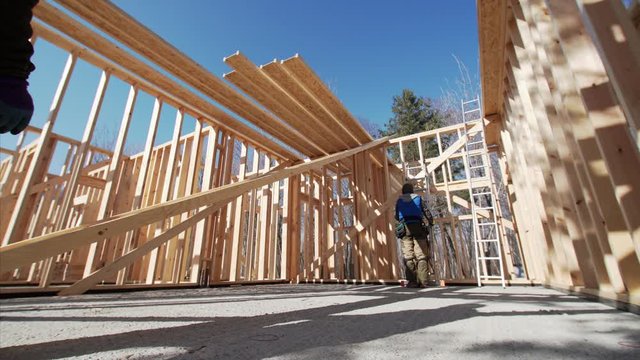 Sliding view of two workers carrying long heavy beam. Frame house site building. Sunny day