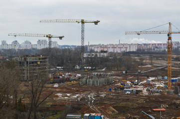 Top view of the construction site during the construction of a new housing estate with tall houses, new buildings with the help of large industrial cranes and professional equipment in a big city