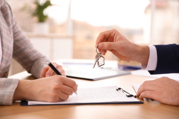 Real estate agent giving key with trinket to client in office, closeup