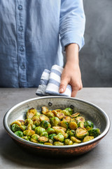 Woman holding pan with roasted Brussels sprouts at light table, closeup