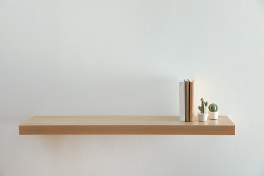 Wooden shelf with books and decorative cactuses on light wall