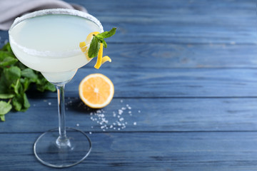 Glass of tasty Margarita cocktail on blue wooden table. Space for text