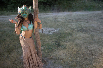 Beautiful tanned girl in the mask of an ancient goddess. The dancer shows movement. Mysterious girl beckons guys. A stranger is looking for a man. Beautiful body of a woman. Unusual high quality mask.