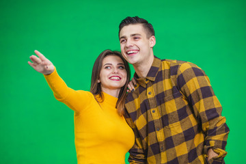 Portrait of happy couple looking and pointing into the distance, isolated on green background.