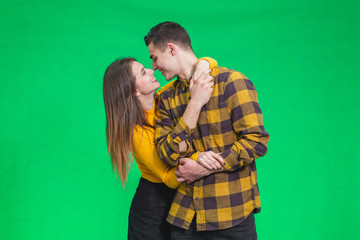 Attractive lovers cuddling, looking one another in eyes, posing on green background.